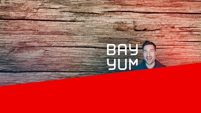 BayYum’s YouTube channel art: weathered wood planks washed red toward the edges, a broad red band rising across the bottom, BAY YUM in white rounded capitals and, beside it, a cut-out of Graham in a dark hoodie, grinning wide