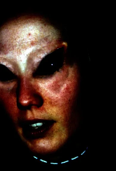 A face in alien makeup: pale skin and huge black eyes