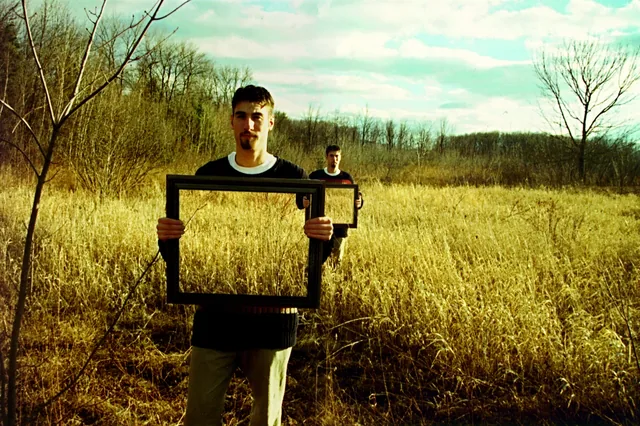 A young man holds up an empty picture frame in a field of tall grass