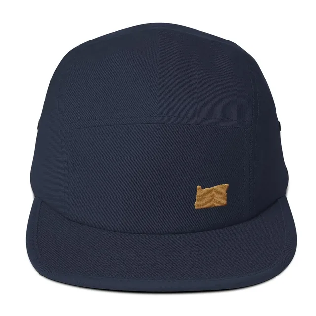 A navy five-panel cap from the front with the Oregon outline embroidered in old-gold thread