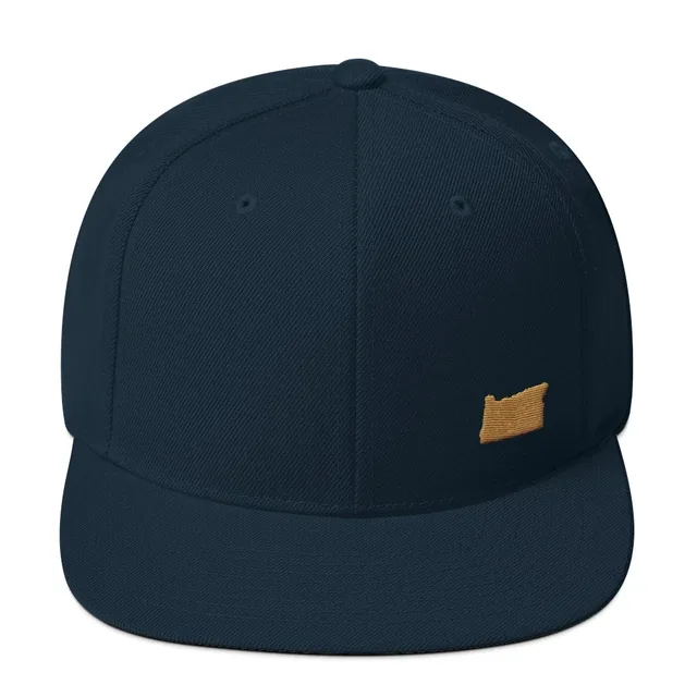 A dark navy snapback cap from the front, with a small outline of Oregon embroidered in old-gold thread low on one side