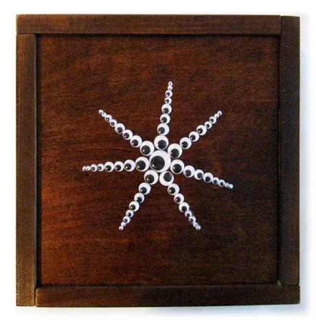 A white starburst of googly eyes on dark wood, in a wooden frame