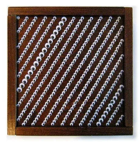 Diagonal lines of googly eyes on dark wood, in a frame