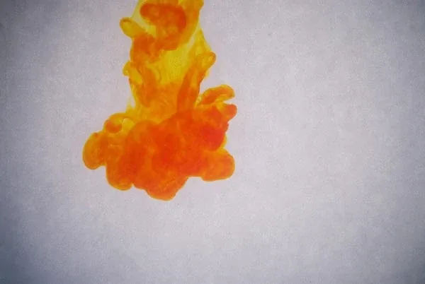 A single plume of orange ink sinking through pale water