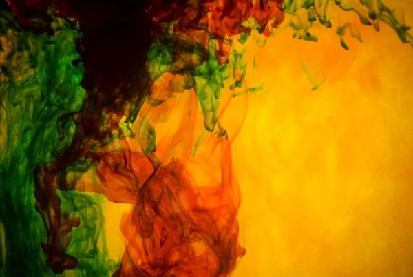 Green, red and orange ink spreading through yellow water