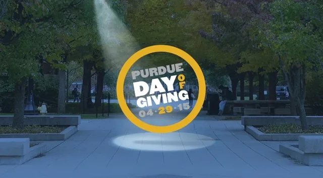 The Purdue Day of Giving logo in a spotlight on a campus walk
