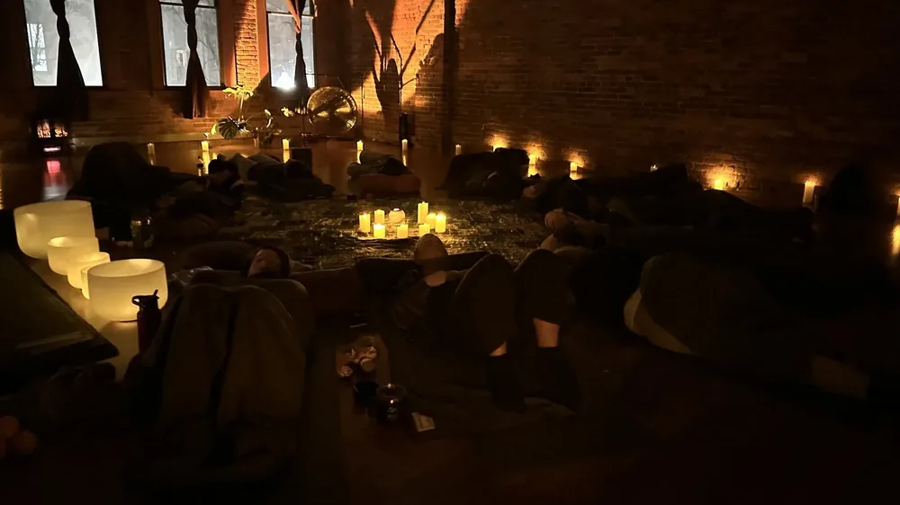 A candlelit Sound Lab at Bodha Yoga: brick walls, tall windows, crystal bowls glowing on the floor